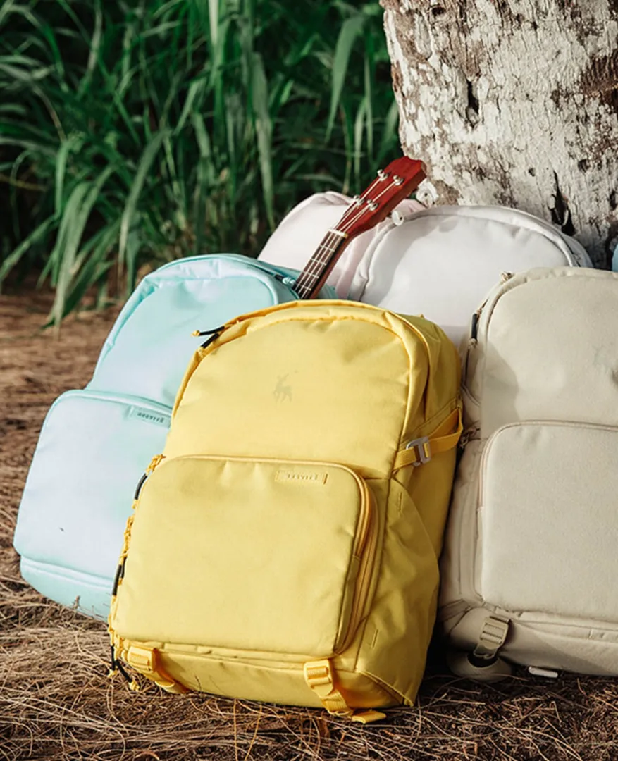 Brevitē backpacks in yellow, teal and cream, leaning against a tree